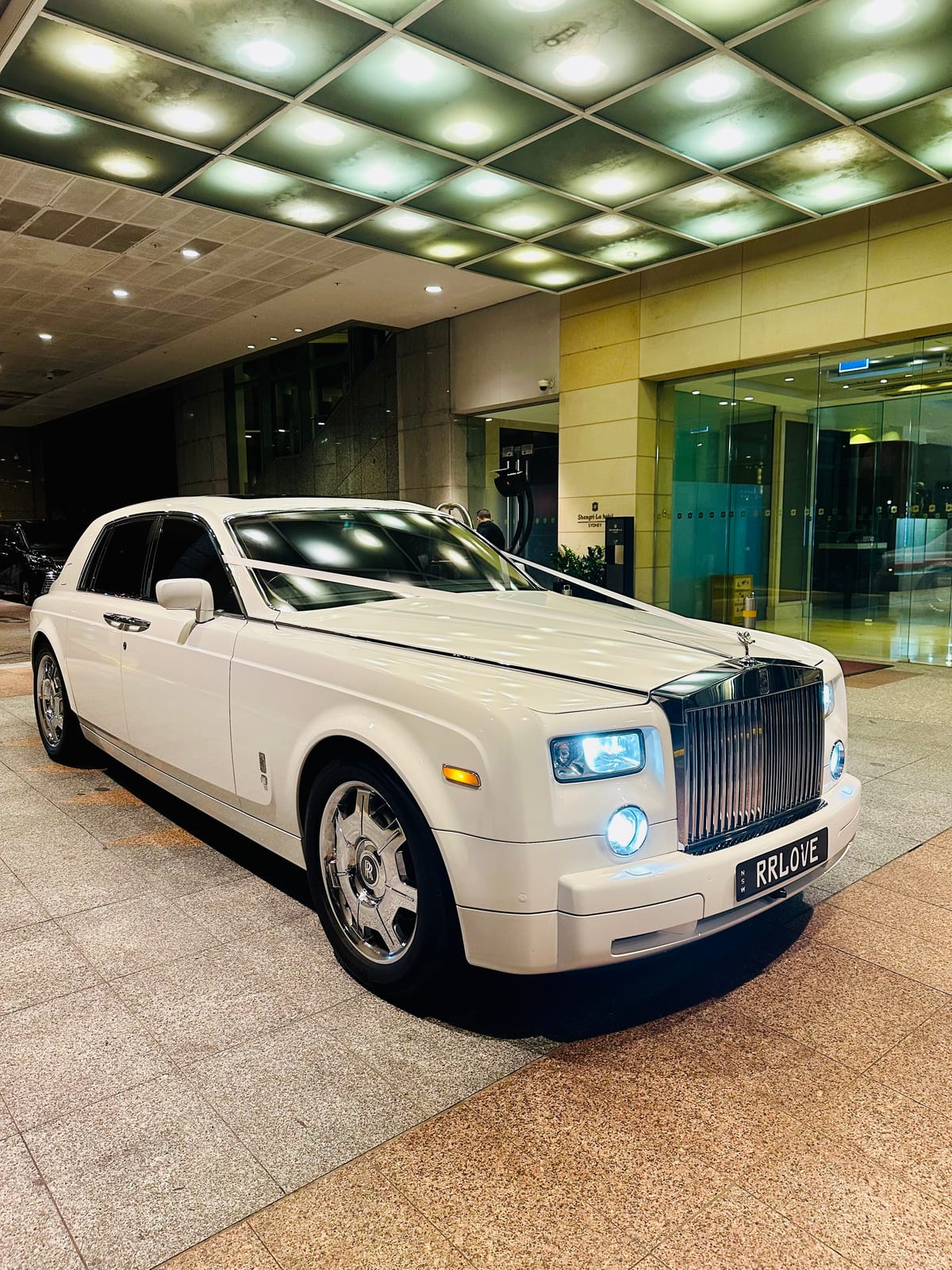 White Rolls Royce Phantom parked at the Shangri-La Sydney hotel entrance at night with headlights on, RRLOVE number plate