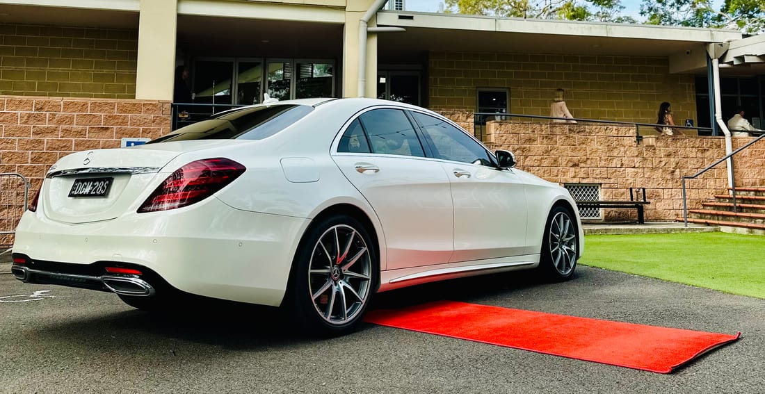 White Mercedes S Class AMG sedan, rear three-quarter, on a red carpet at a venue